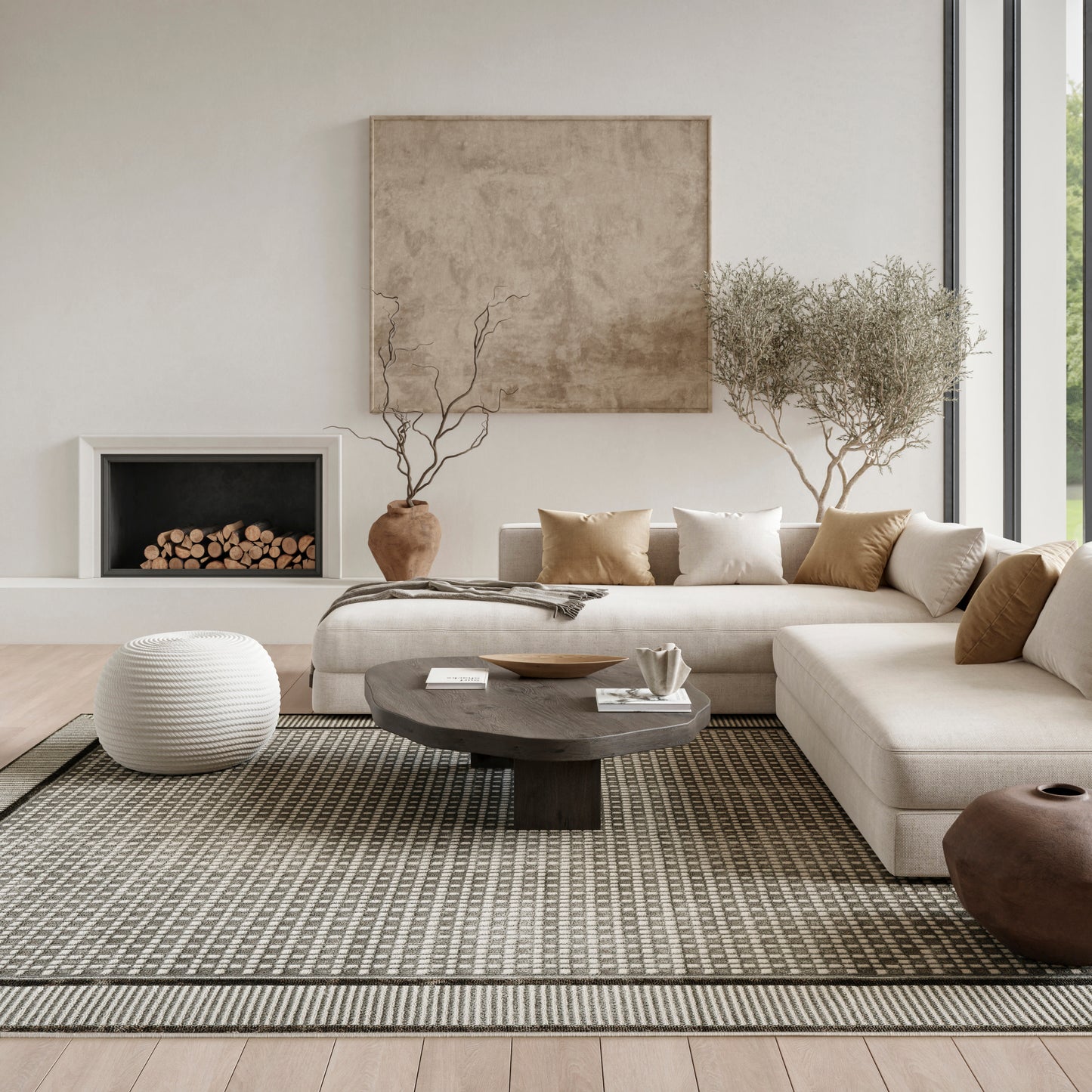 Neutral living room with beige sectional, round dark coffee table, white knit pouf, rug, fireplace, and potted trees.