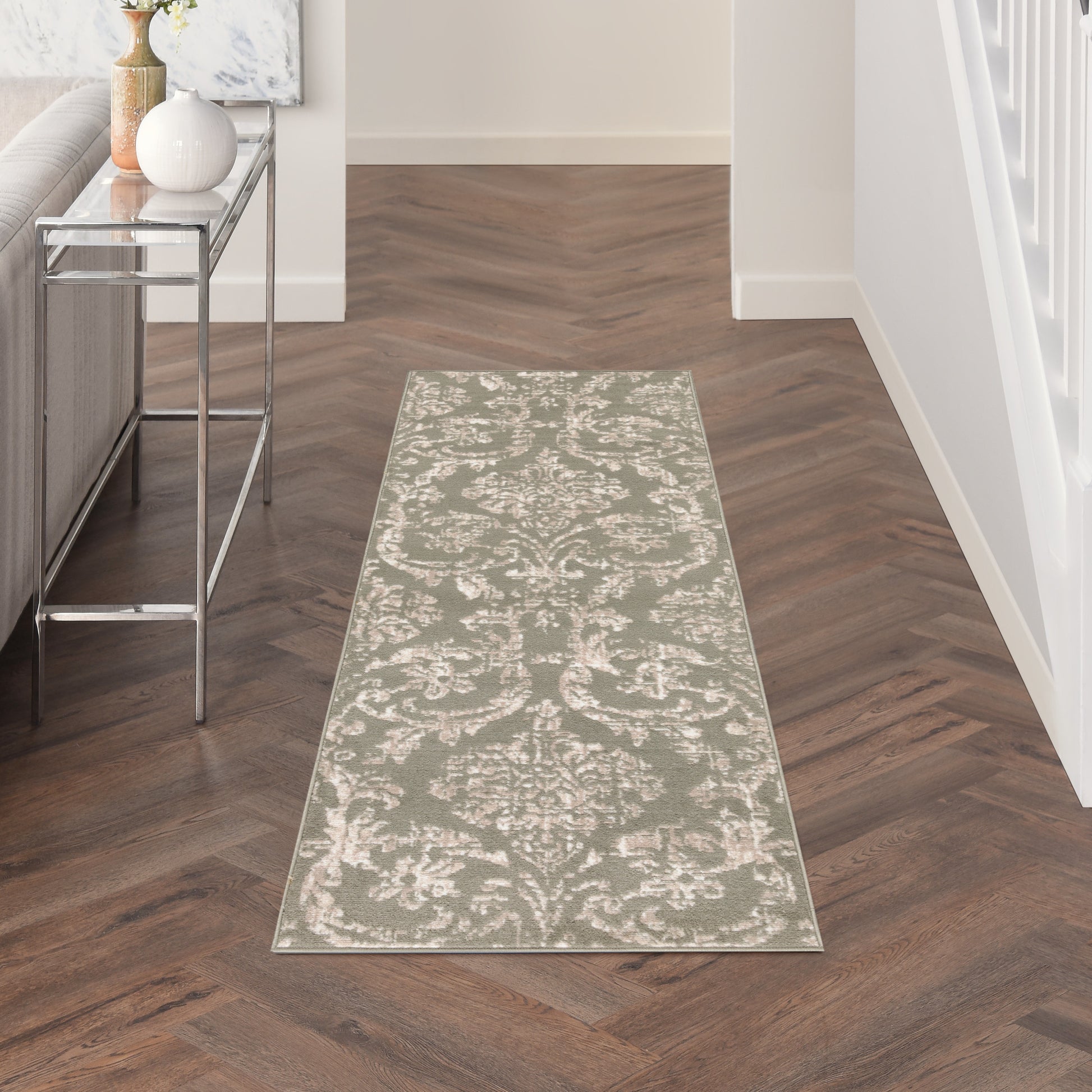 Long damask-patterned runner rug in beige and ivory on dark wood hallway floor with a metal-framed glass console.