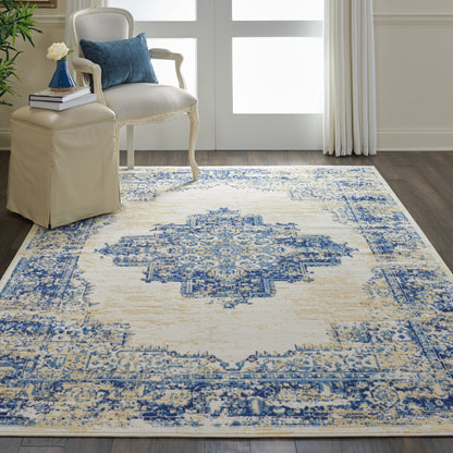 Blue and ivory distressed oriental rug with central medallion on dark wood floor; cream carved-armchair, blue cushion, beige ottoman.