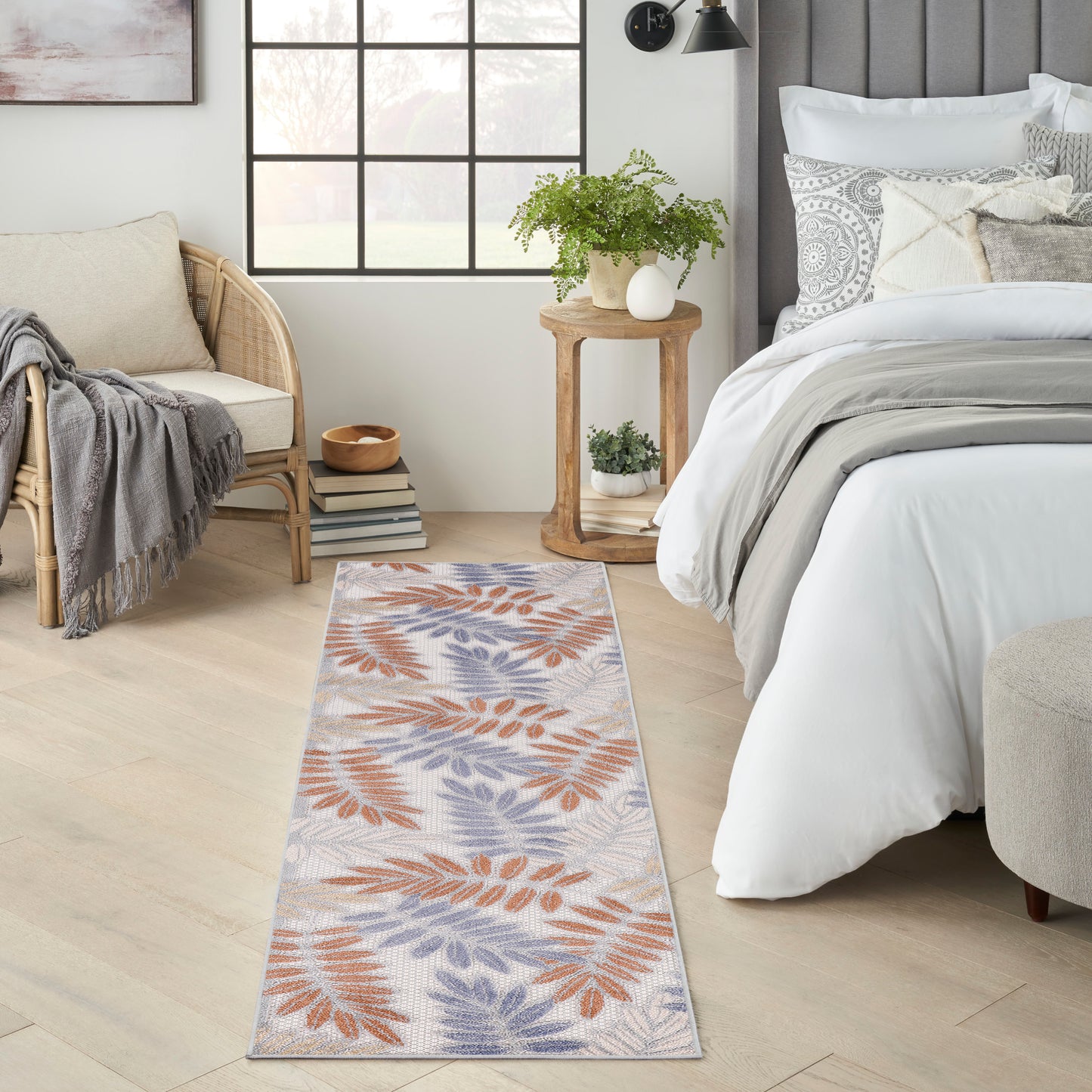 Long woven rug runner with orange and blue leaf pattern on beige, placed in a light modern bedroom beside the bed.