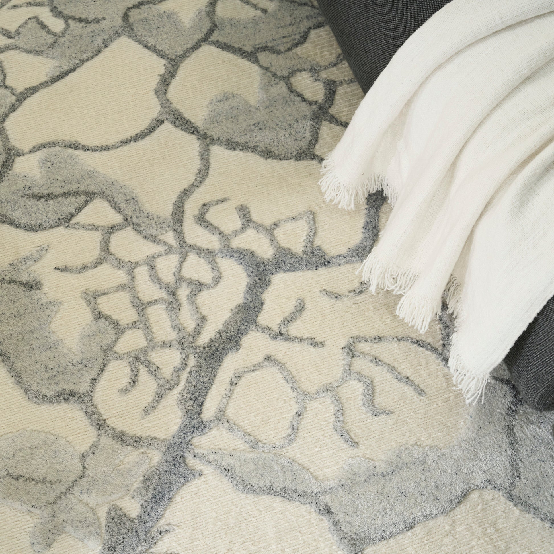 Beige & gray abstract-pattern area rug with plush pile; white fringed throw draped over edge.