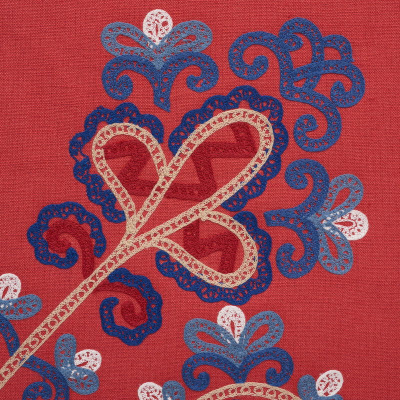 Vermilion fabric with blue and white lace-like floral embroidery; a cream lace-looped ribbon motif over paisley-style shapes.