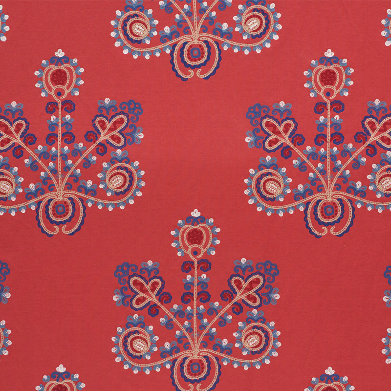 Red fabric with blue and white ornate paisley floral motifs in a repeating pattern.