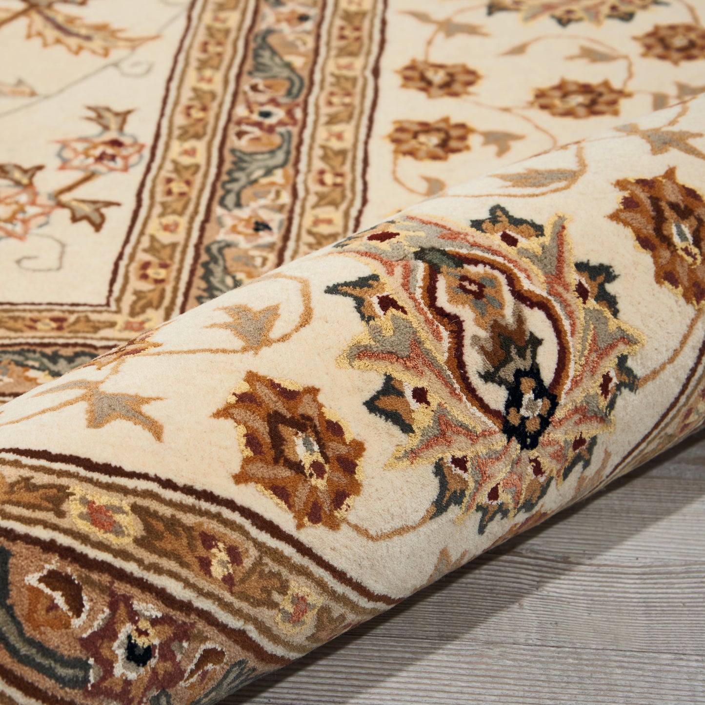 Beige Persian-style rug with ornate floral border in brown, cream and blue; rolled corner and soft pile.