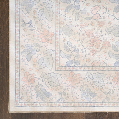 Pastel floral woven area rug with blue, peach and ivory tones, bordered pattern on light beige, laid on wood floor.