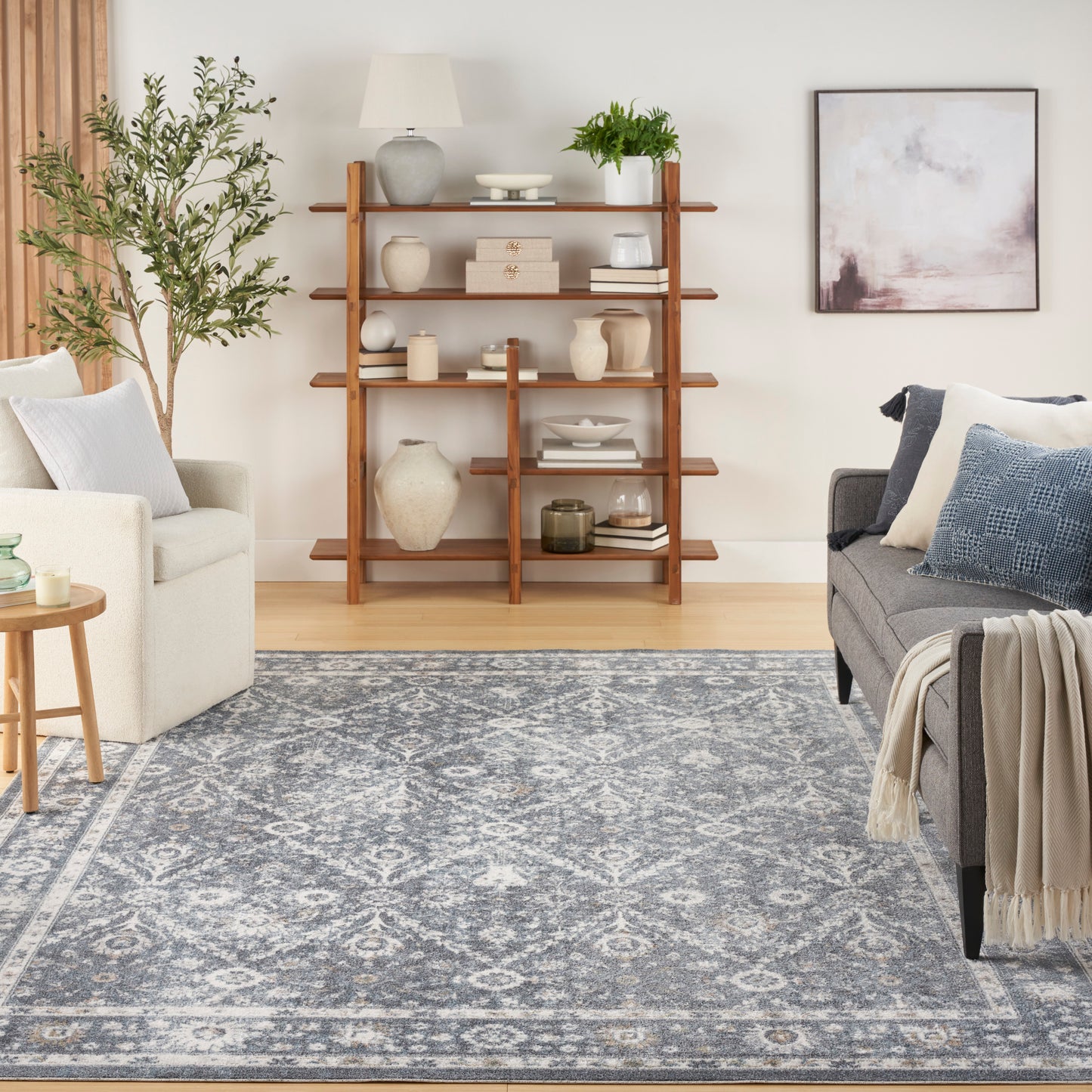 Cozy living room with a wooden four-tier ladder shelf of ceramic vases, blue-gray patterned rug, gray sofa and beige armchair