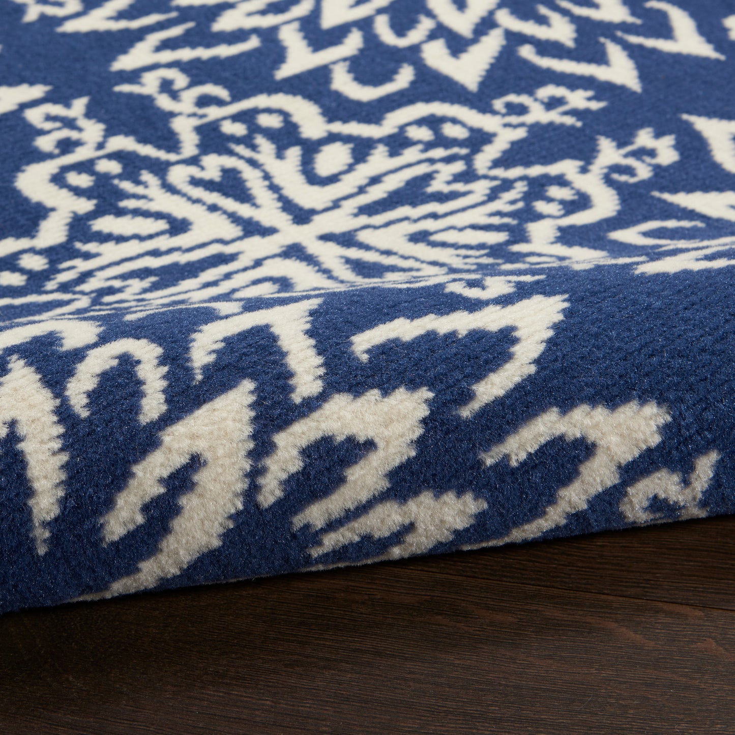 Blue rug with white Nordic snowflake pattern, plush wool-like texture, folded corner on dark wood floor.