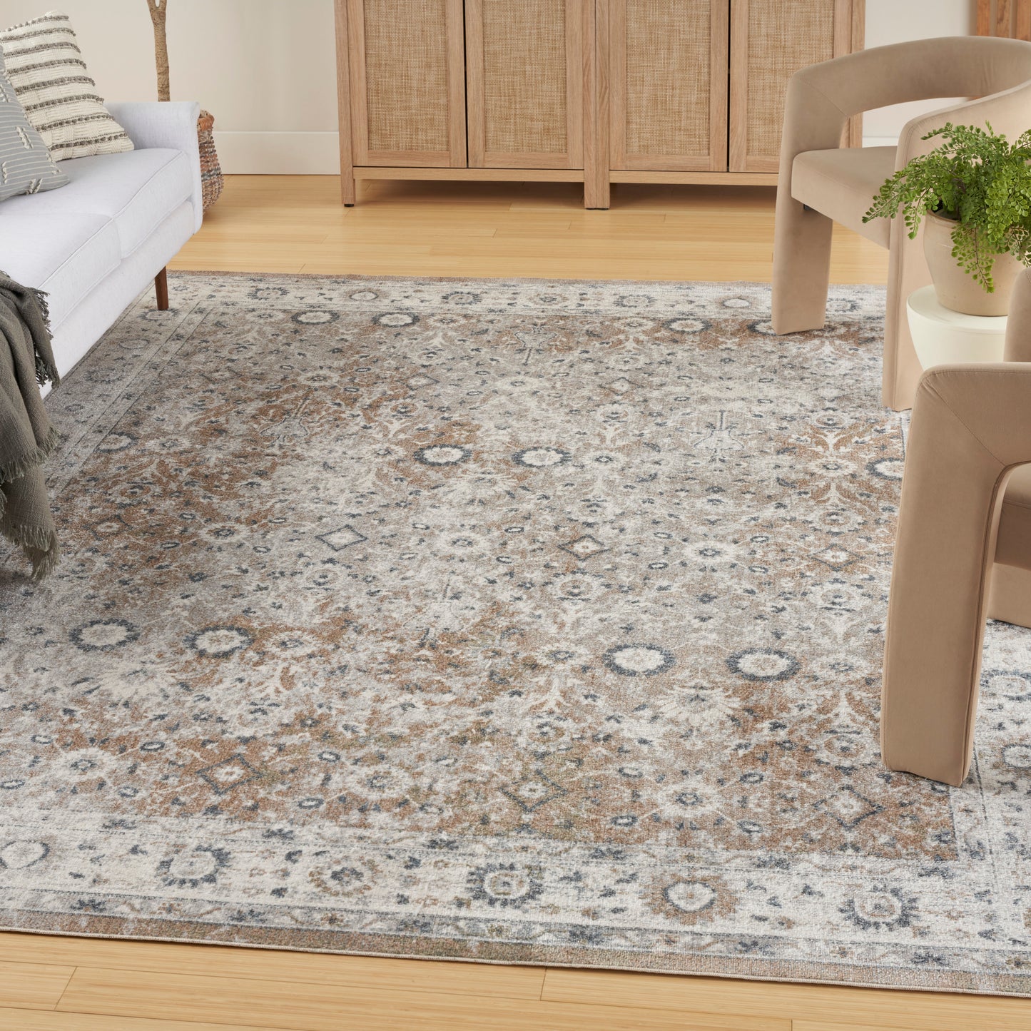 Living room with a large beige-blue patterned area rug on light hardwood; gray sofa left, beige chairs right, wooden cabinet at back.