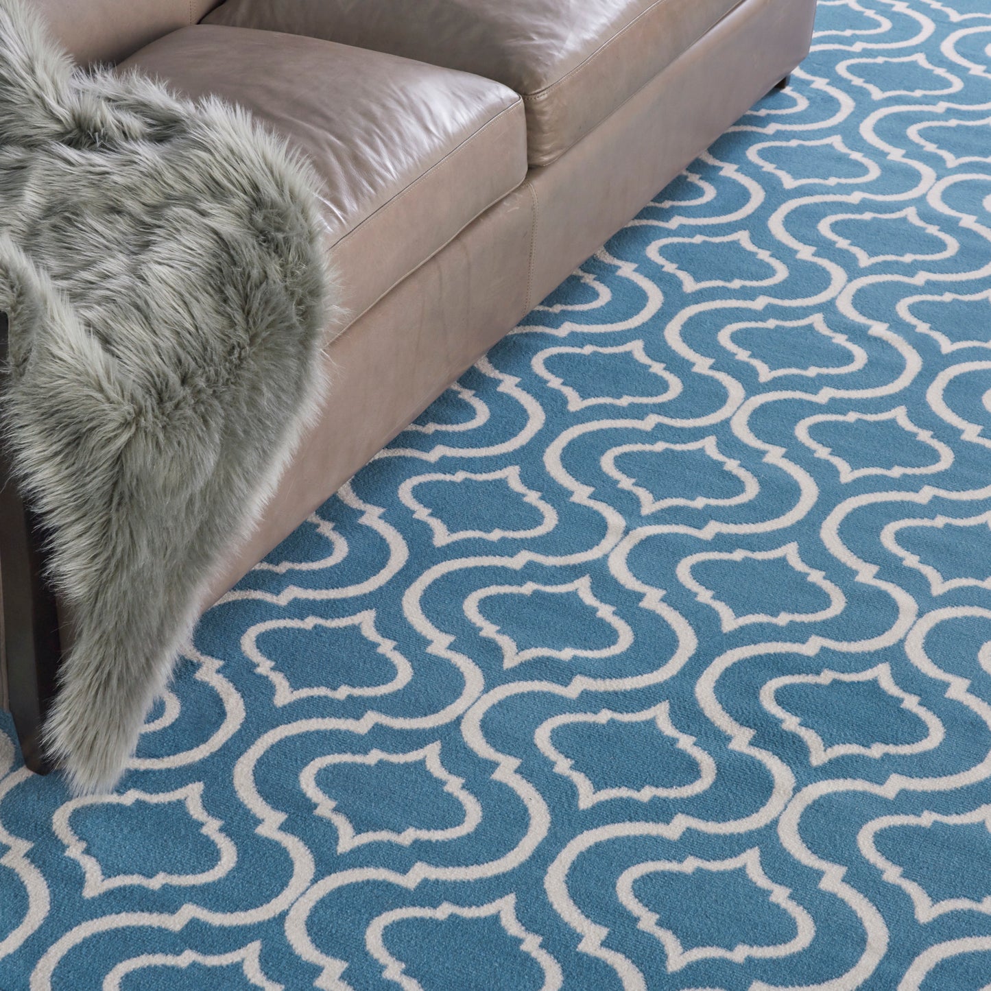 Blue trellis-pattern area rug with white motifs under a beige sofa and a gray faux fur throw.