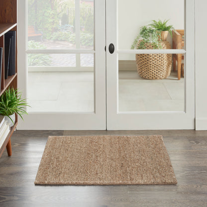 Rectangular natural jute entry rug on dark wood floor in front of white-framed glass French doors; rustic coastal style.