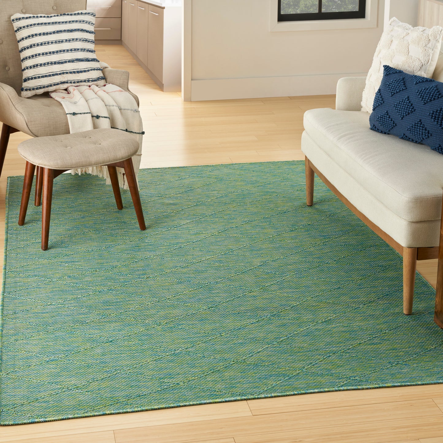 Teal woven area rug with subtle pattern under mid-century beige armchair and ottoman beside cream sofa with blue pillow.