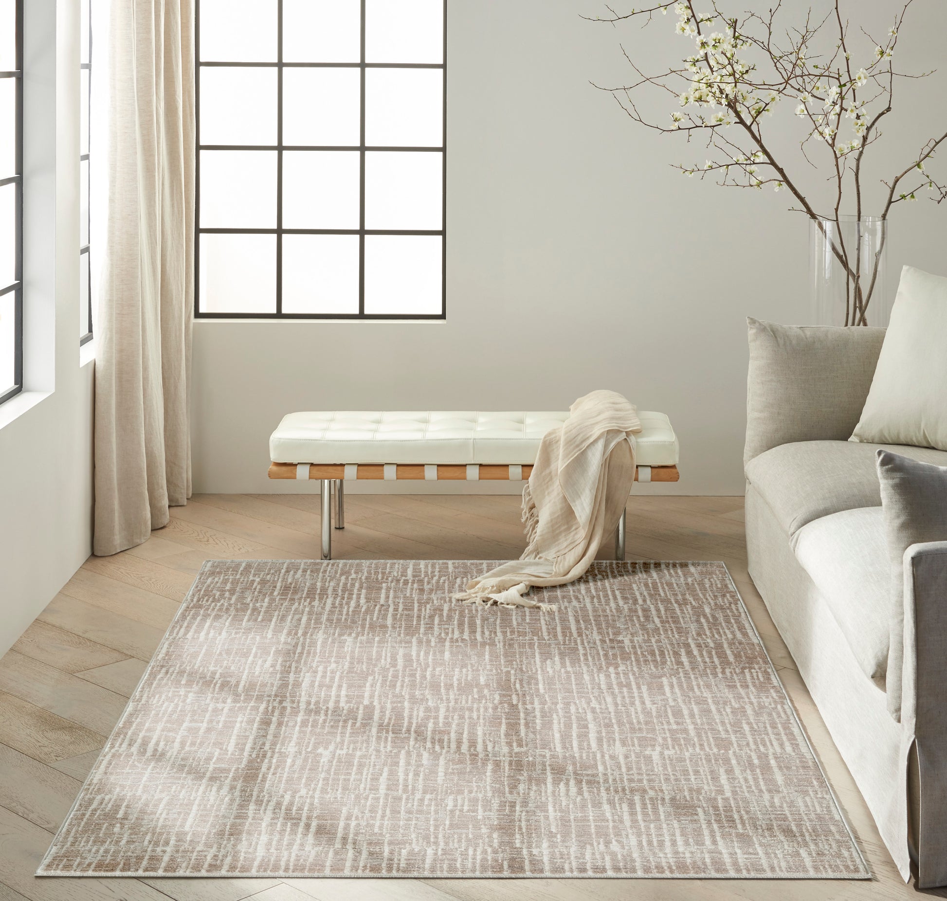 Neutral living room with beige textured rug, white tufted bench, sheer curtains and a gray sofa.