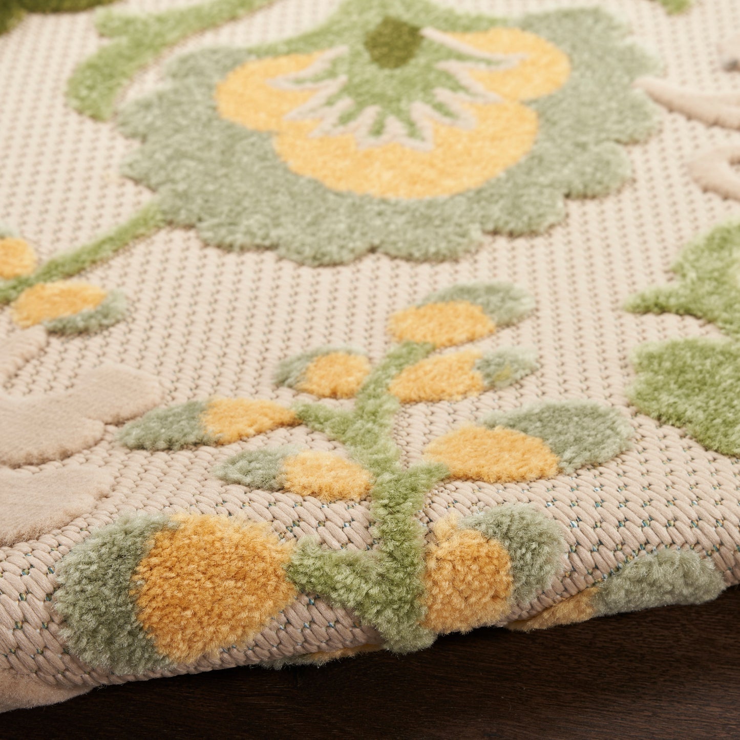 Beige round outdoor rug with a raised green and yellow floral motif; tufted, plush pile.