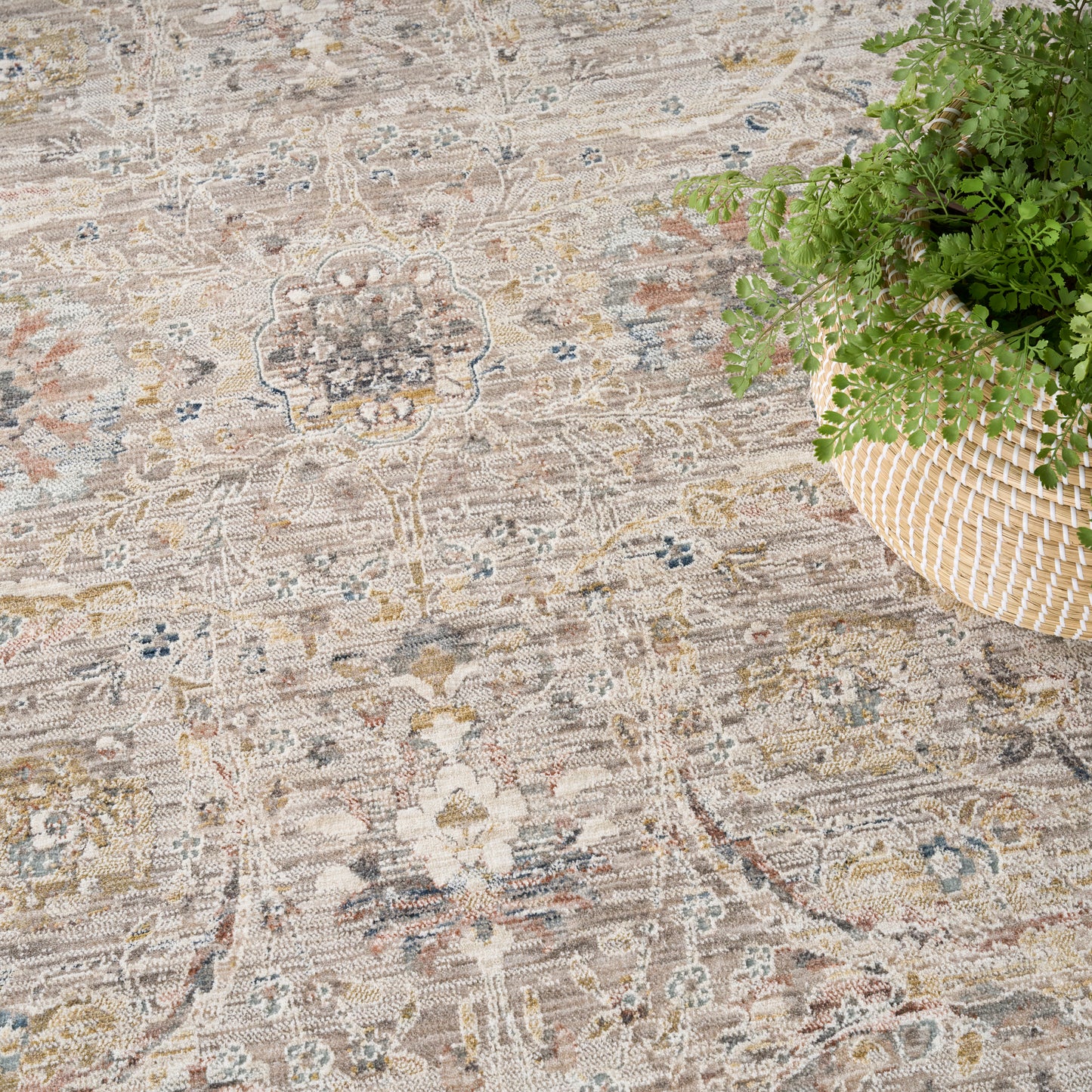 Beige vintage-style rug with a faded floral medallion pattern and subtle blue accents, on a floor beside a woven basket plant