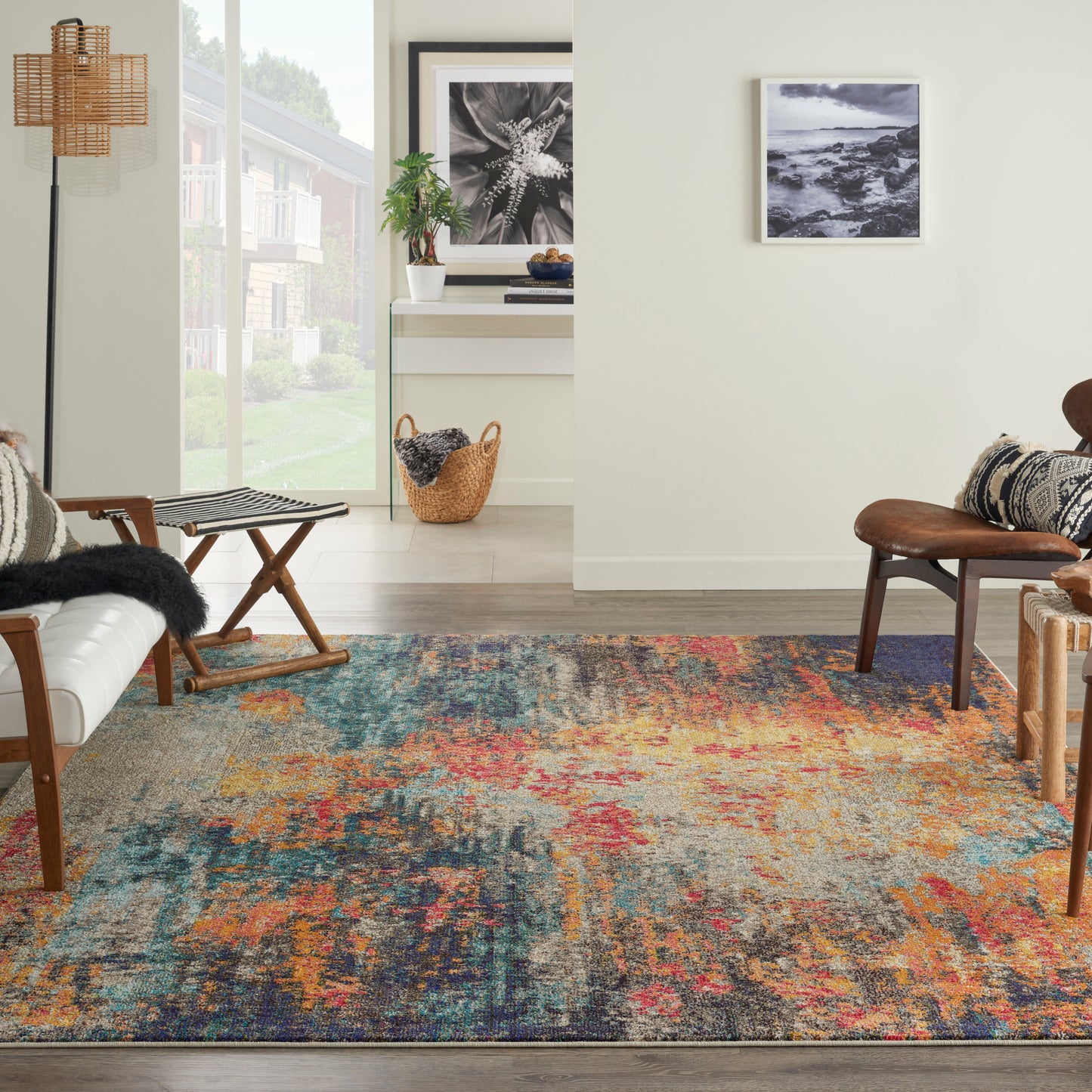 Bright living room with a multicolor blue-orange-pink rug, mid-century leather chair, wicker basket, and black-and-white art.