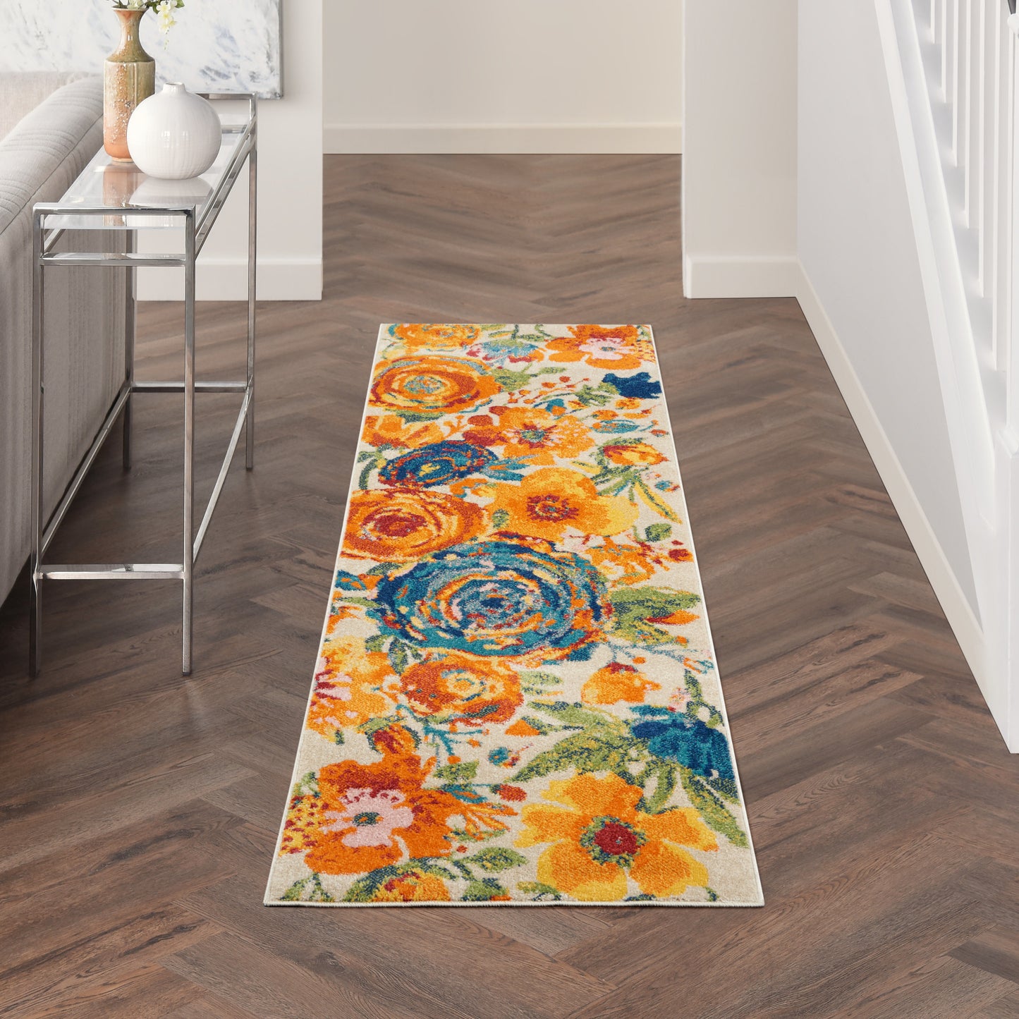 Floral runner rug with orange, yellow and blue blooms in a hallway beside a glass console table.