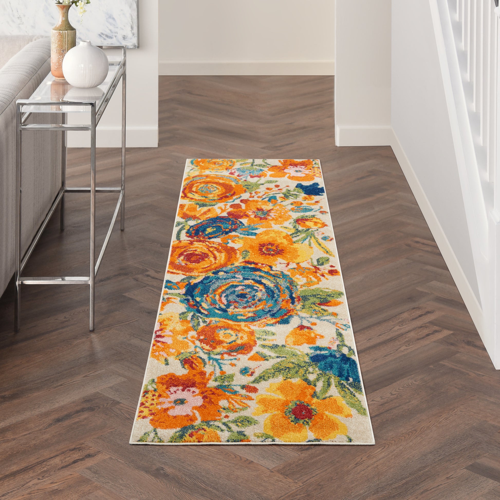 Floral runner rug with orange, yellow and blue blooms in a hallway beside a glass console table.
