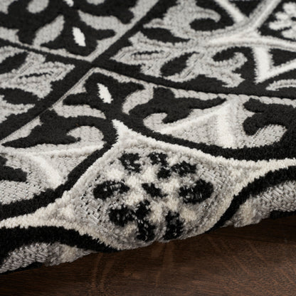 Plush black and white damask-pattern rug with thick cut pile, curled edge on dark wood floor.