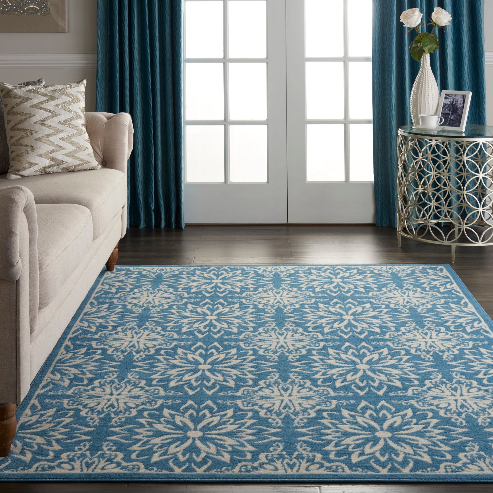 Blue area rug with white floral medallion pattern in a living room with a beige sofa and teal drapes.