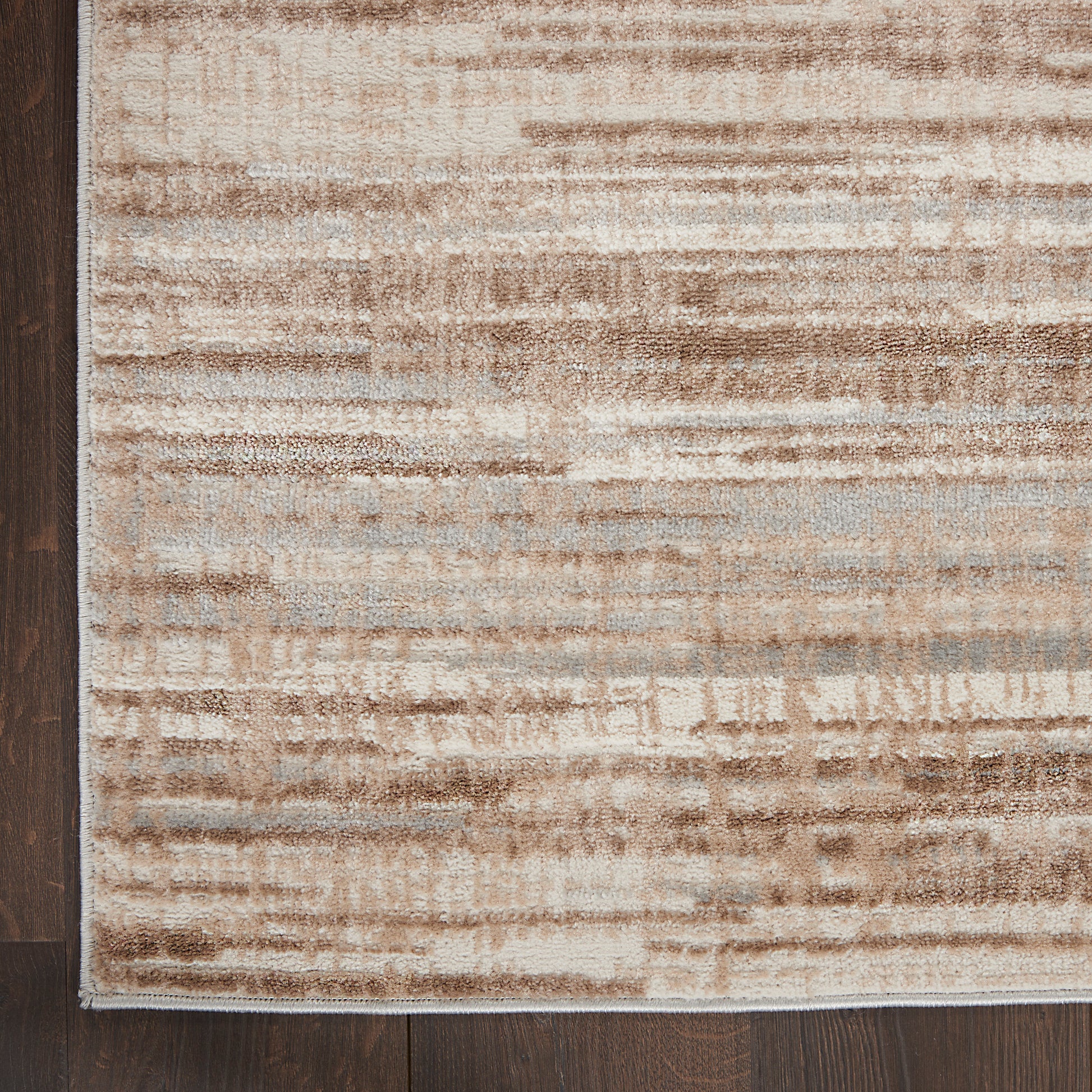 Low-pile area rug in beige, tan and blue-gray with a distressed striped pattern on dark wood floor.