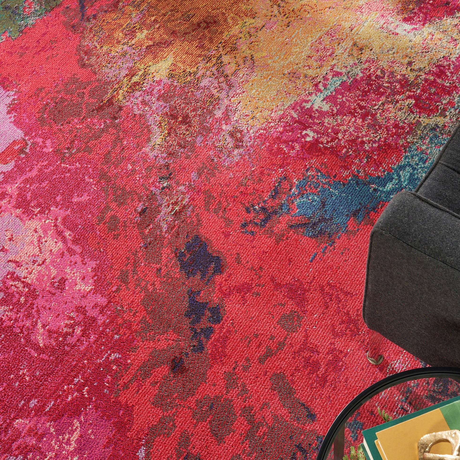 Abstract multicolor area rug in red, pink, orange and blue tones beside a dark gray sofa and round glass coffee table.