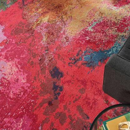 Abstract multicolor area rug in red, pink, orange and blue tones beside a dark gray sofa and round glass coffee table.