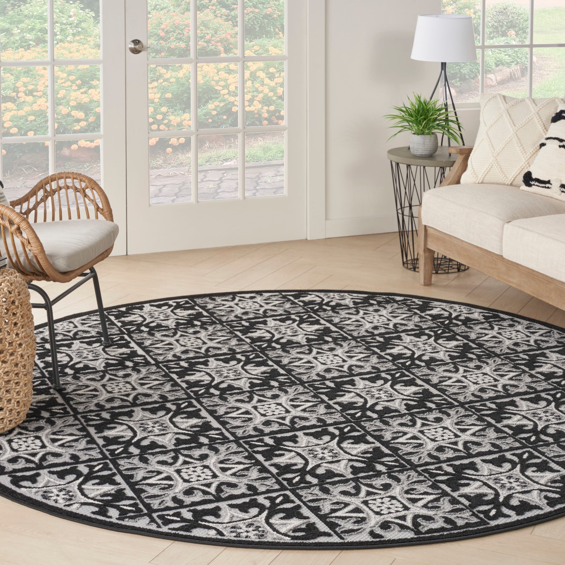 Round black and ivory patterned area rug in a bright living room with wicker chair, beige sofa, and indoor plants.