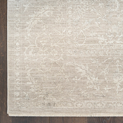 Beige oriental area rug with subtle floral motif, cream fringe along edge & laid on dark wood floor.