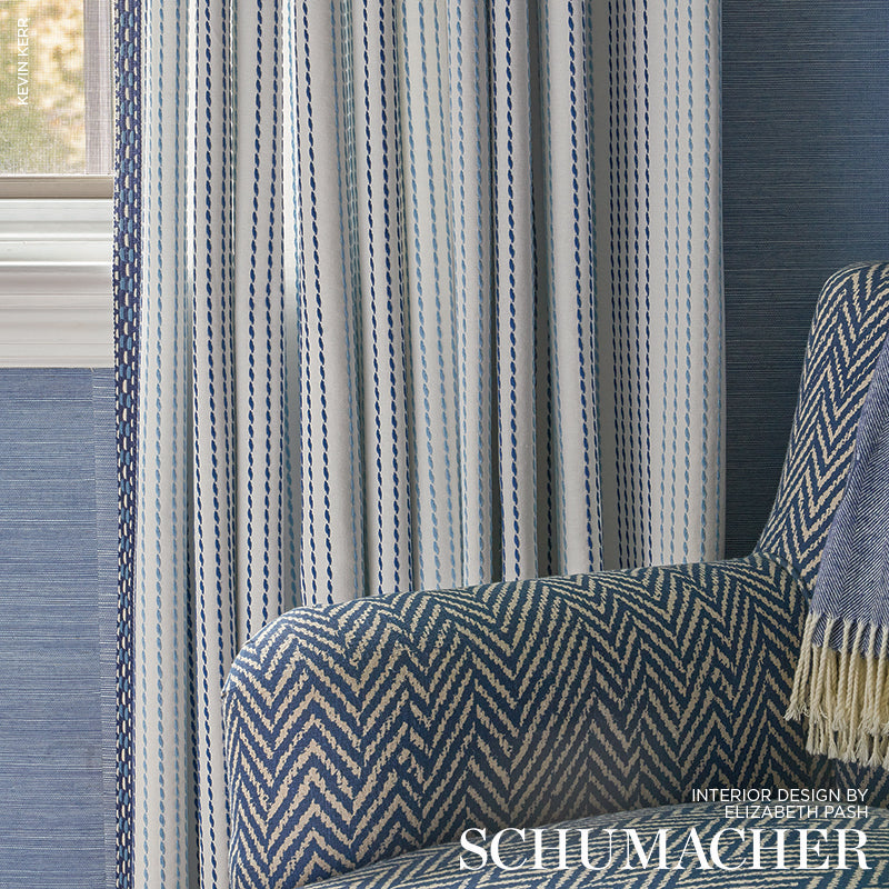 Blue & white chevron upholstered armchair beside vertical striped blue curtains in a cozy living room.