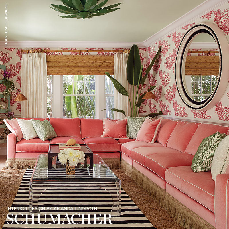 Pink velvet sectional sofa in a tropical living room with damask wallpaper, zebra rug, and round mirror.