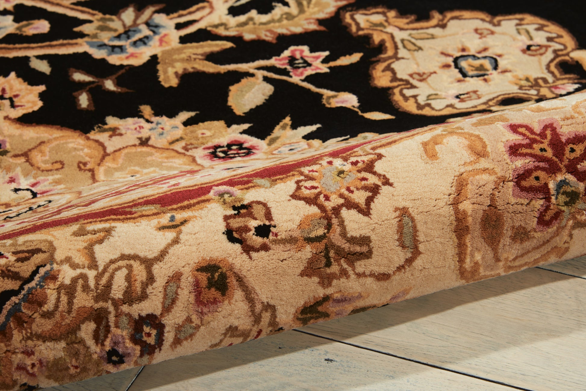 Close-up view of an ornate oriental rug edge with cream, black & gold floral pattern; pink border on a wooden floor.