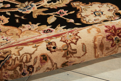 Close-up view of an ornate oriental rug edge with cream, black & gold floral pattern; pink border on a wooden floor.