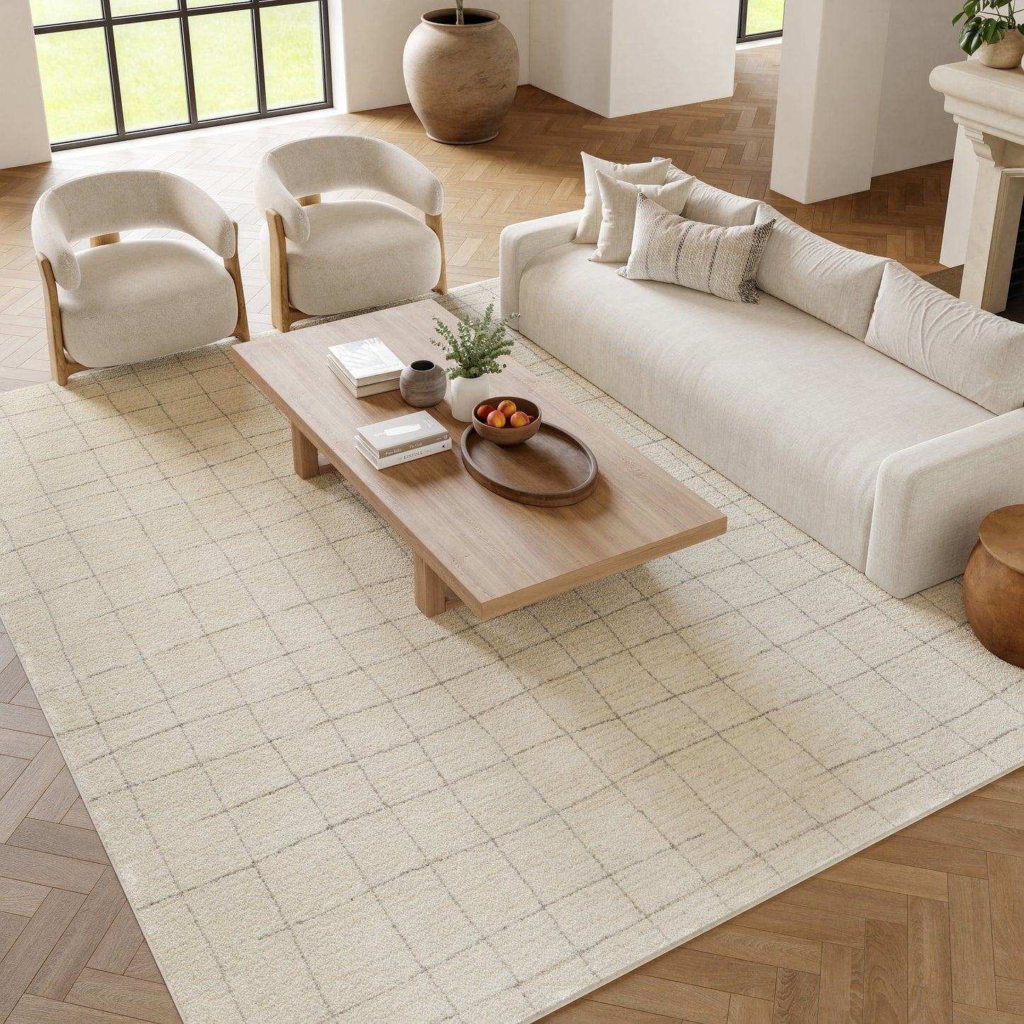 Modern living room with cream sofa, two curved beige armchairs, low wooden coffee table on a pale grid rug.