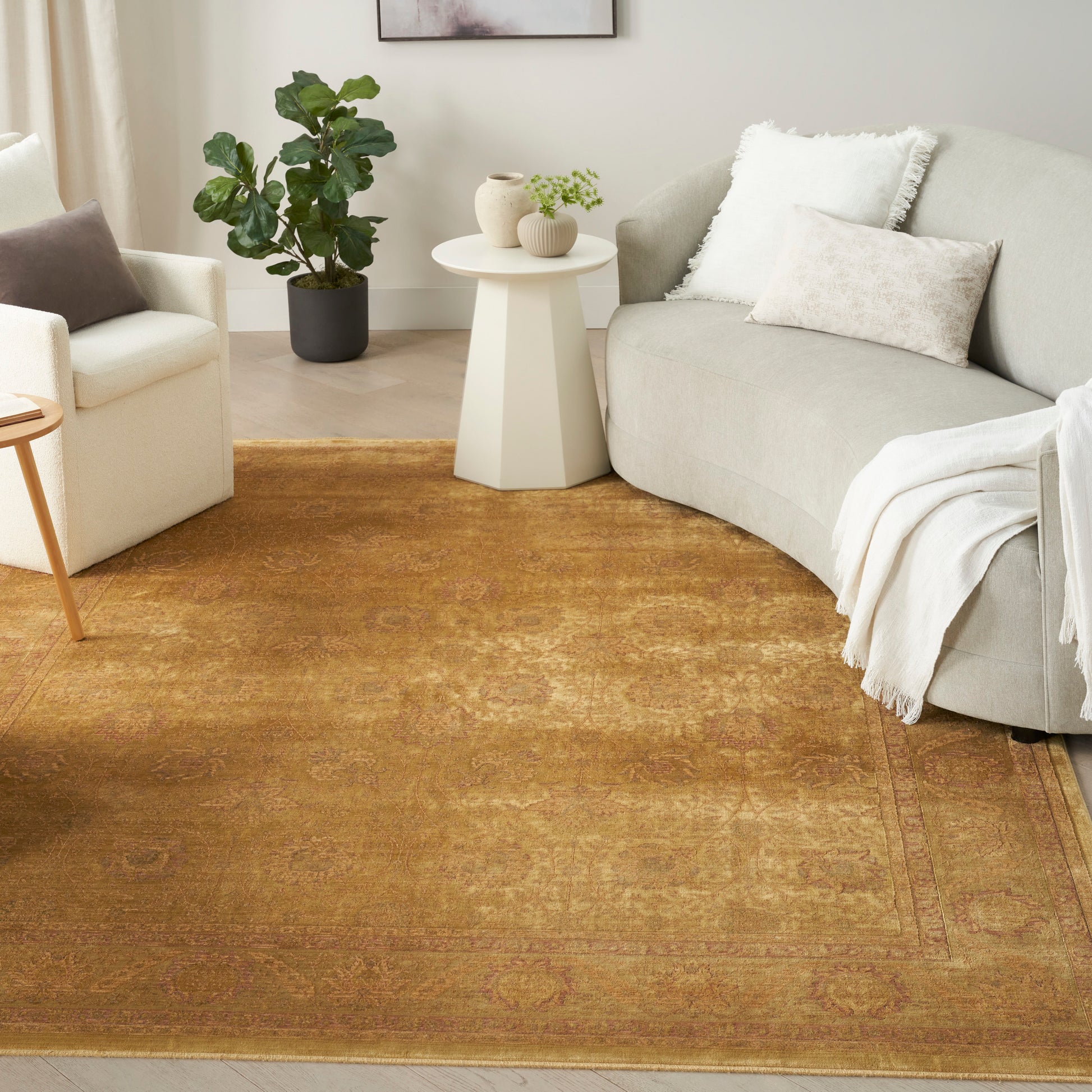 Cozy living room with tan-gold oriental rug, curved beige sofa, white throw, round white side table and potted plant.