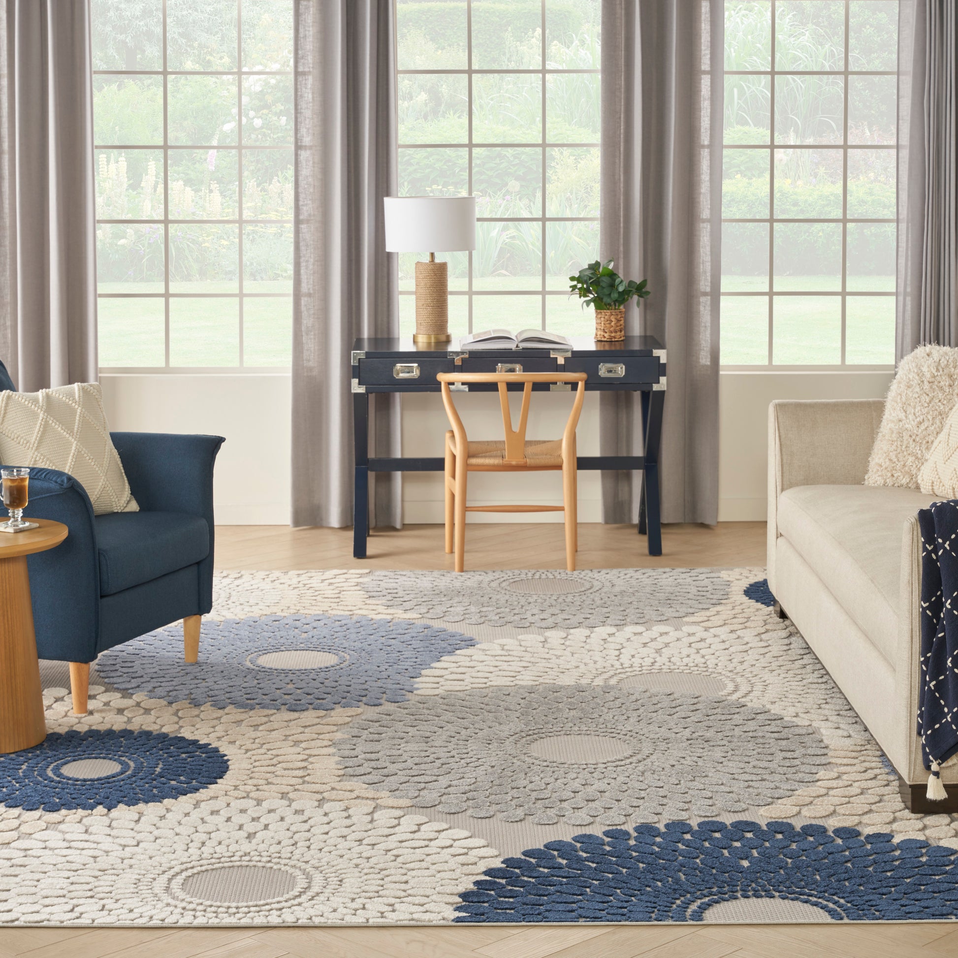 Cozy living room with navy desk, light wood chair, gray sofa, blue armchair, circular gray-blue rug, open book.