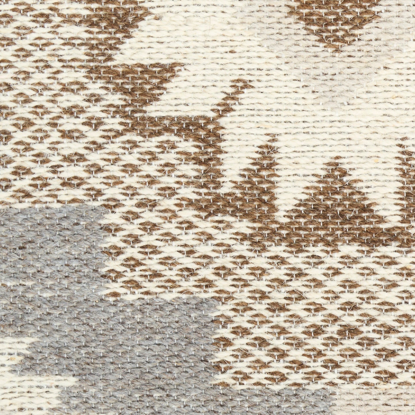 Close-up of a beige-brown geometric modern rug with a grey-blue patch; a textured woven pattern.
