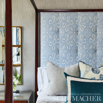 Blue damask-patterned wall panel with a dark wood frame, seen behind a white bed with beige and teal cushions.