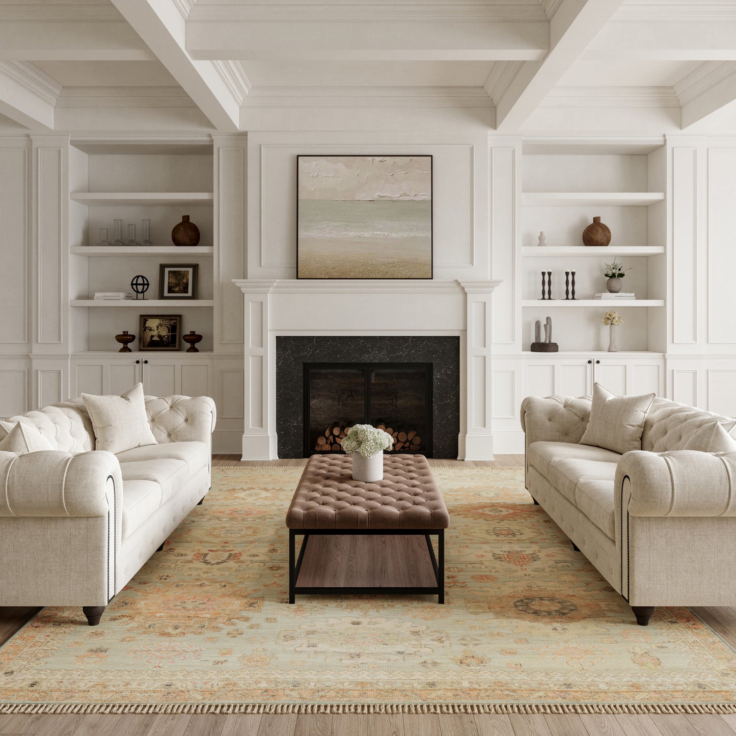 Neutral rug in a living room with white paneled walls, a fireplace, two beige tufted sofas, a brown ottoman, and a framed seascape above the mantel.