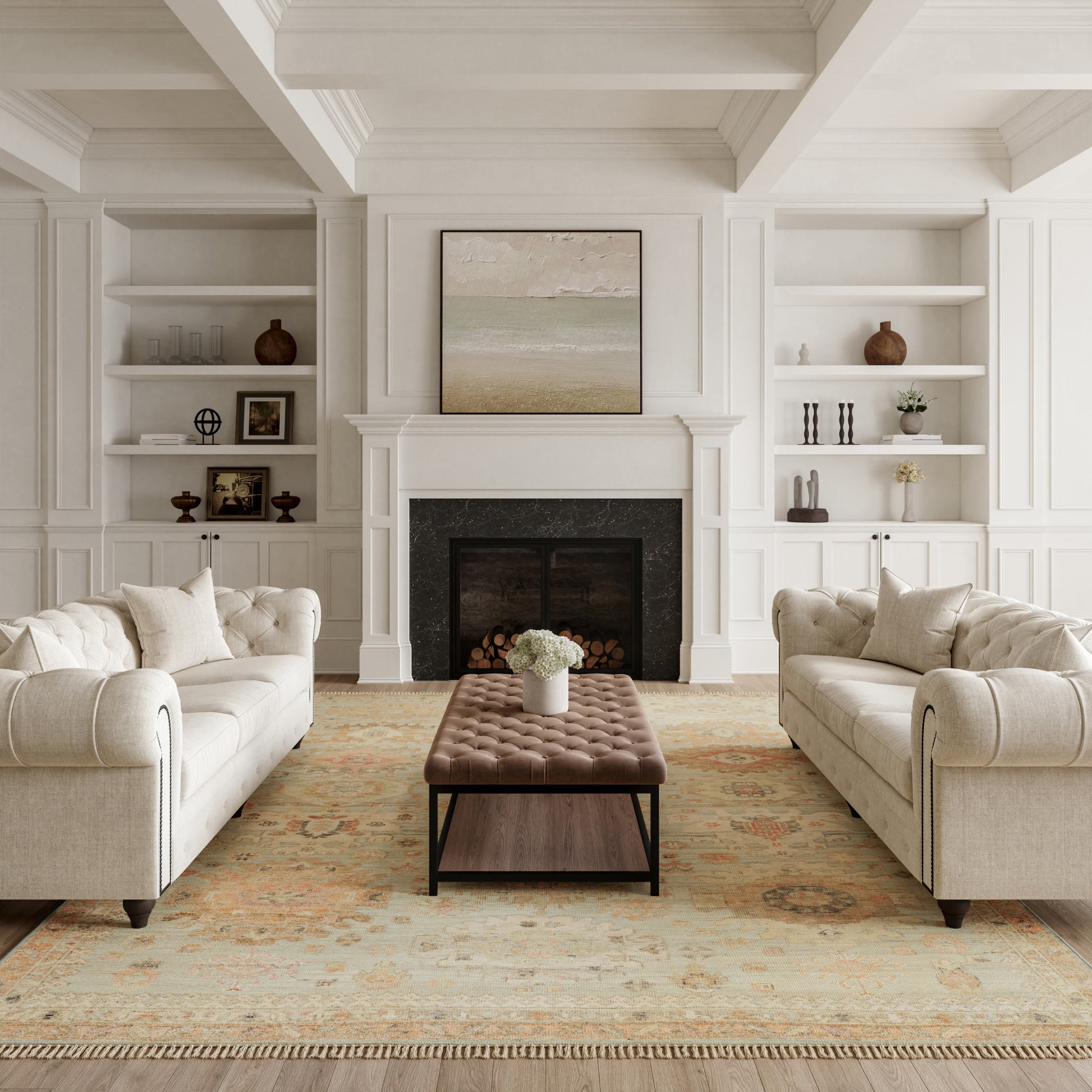 Neutral rug in a living room with white paneled walls, a fireplace, two beige tufted sofas, a brown ottoman, and a framed seascape above the mantel.
