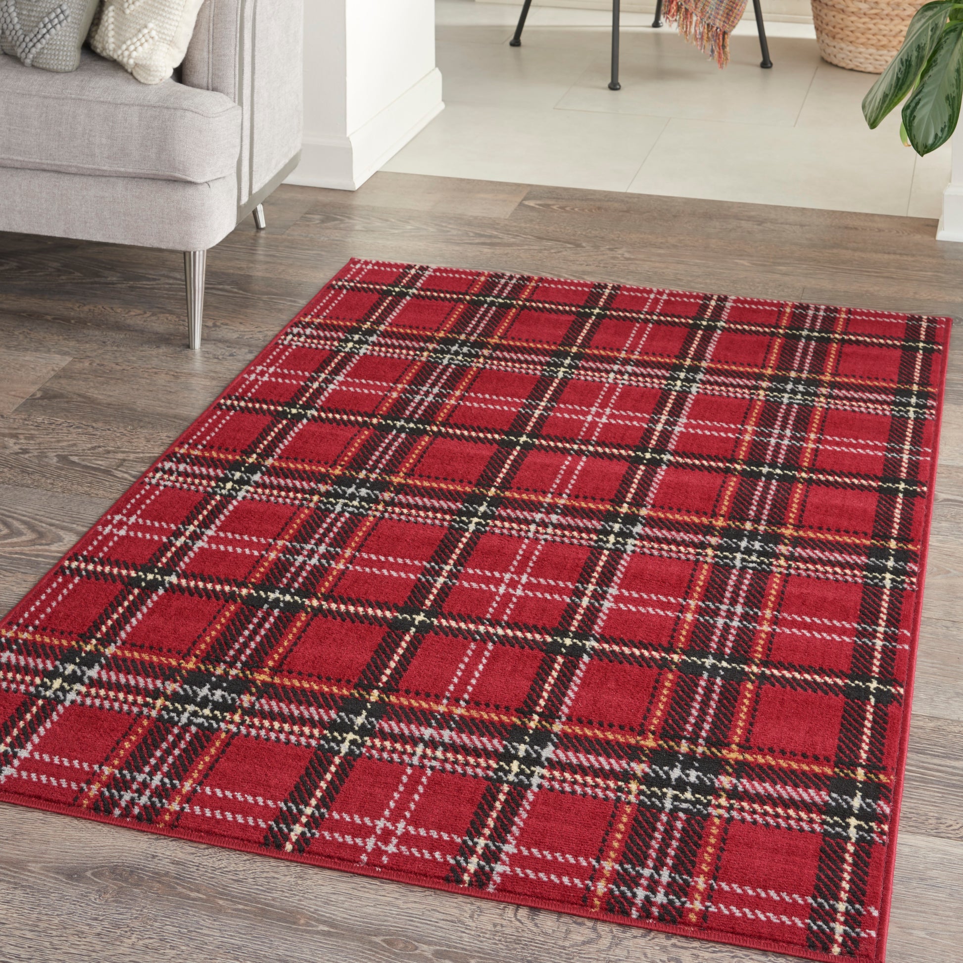 Red plaid area rug with black and white accents on dark wood floor in a cozy living room.