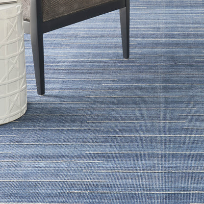 Blue striped rug with denim tones, black metal chair leg, and white latticed side table.