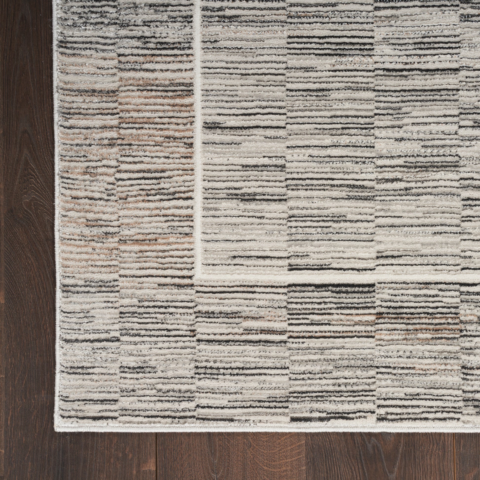 Neutral patchwork rectangular area rug with cream, beige, taupe and gray stripes on dark wood floor.