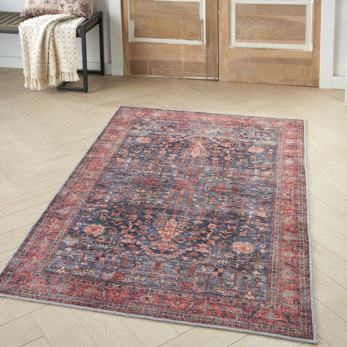 Persian-style Oriental rug with navy blue field, red floral medallions, and layered red/ivory borders on light wood floor.