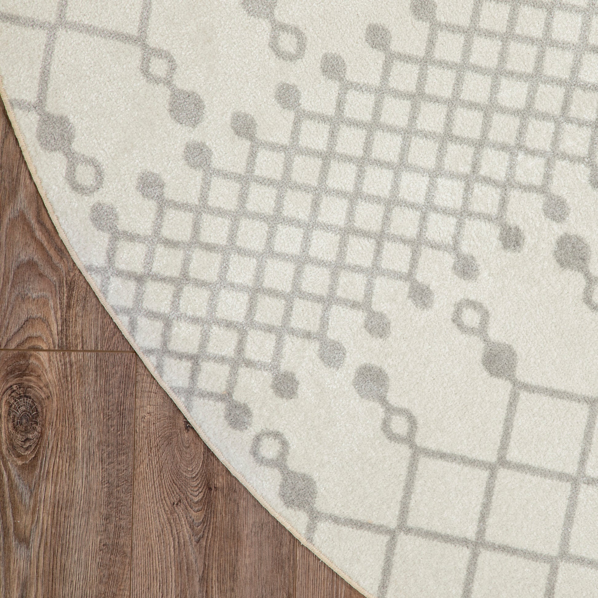 Beige round area rug with gray geometric grid & dot accents on warm wood flooring.