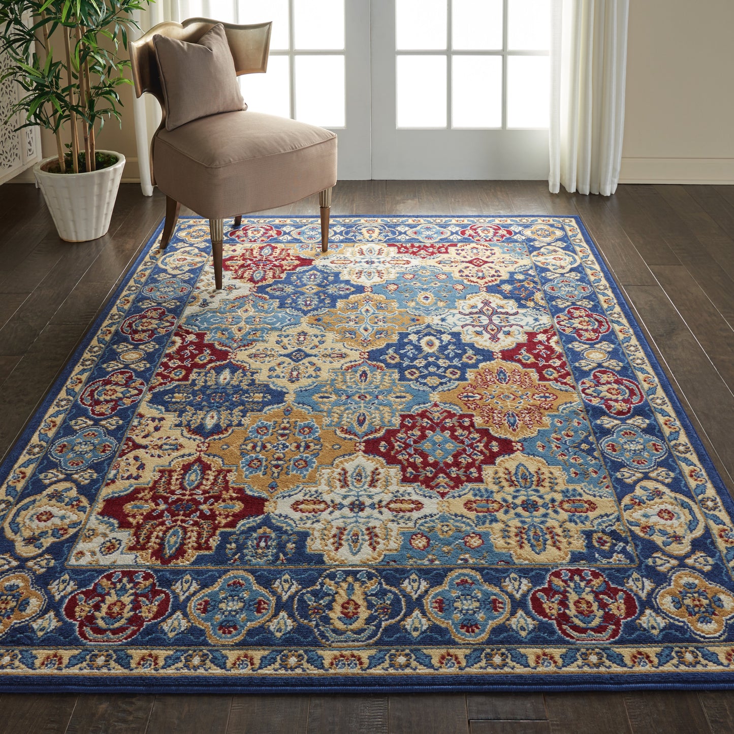 Oriental-style area rug with blue border and colorful medallions in red, cream and gold on dark wood floor near blush chair