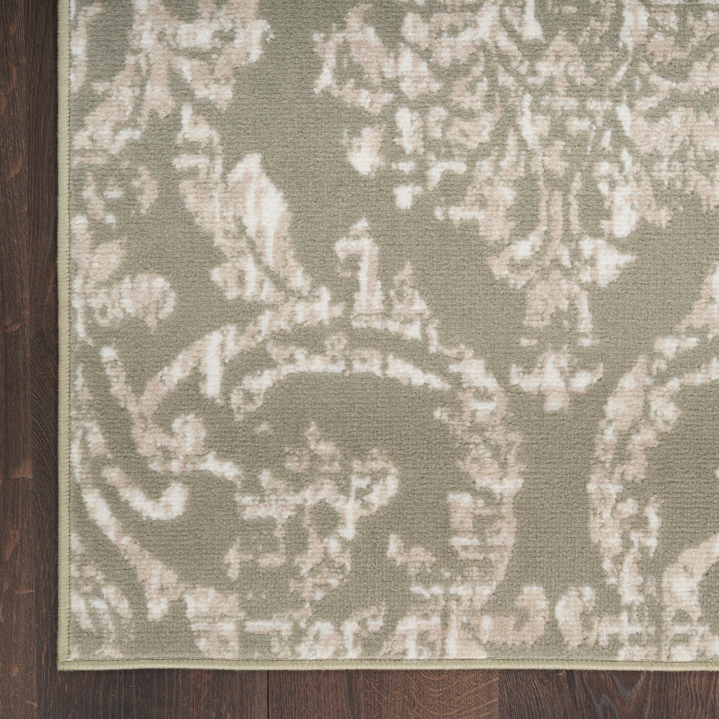 Muted sage rug with ivory damask pattern and dark wood trim along left edge.