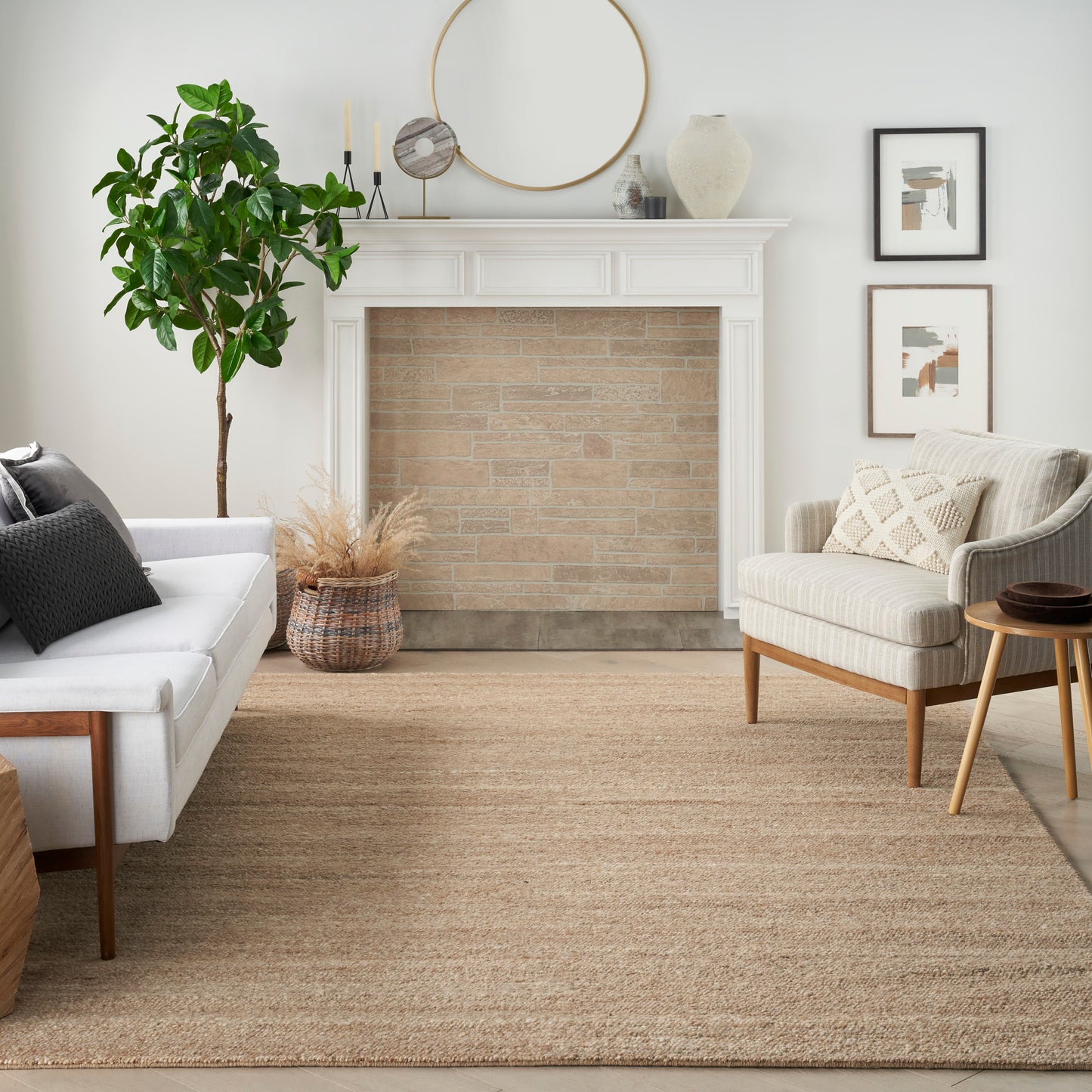 Neutral living room with white mantel & round mirror, beige brick inset, green fiddle-leaf fig, cream sofa & beige armchair, jute rug.