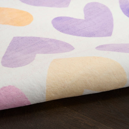 Soft cotton fabric with pastel lavender, peach and pink hearts on white, folded on a dark wooden surface.