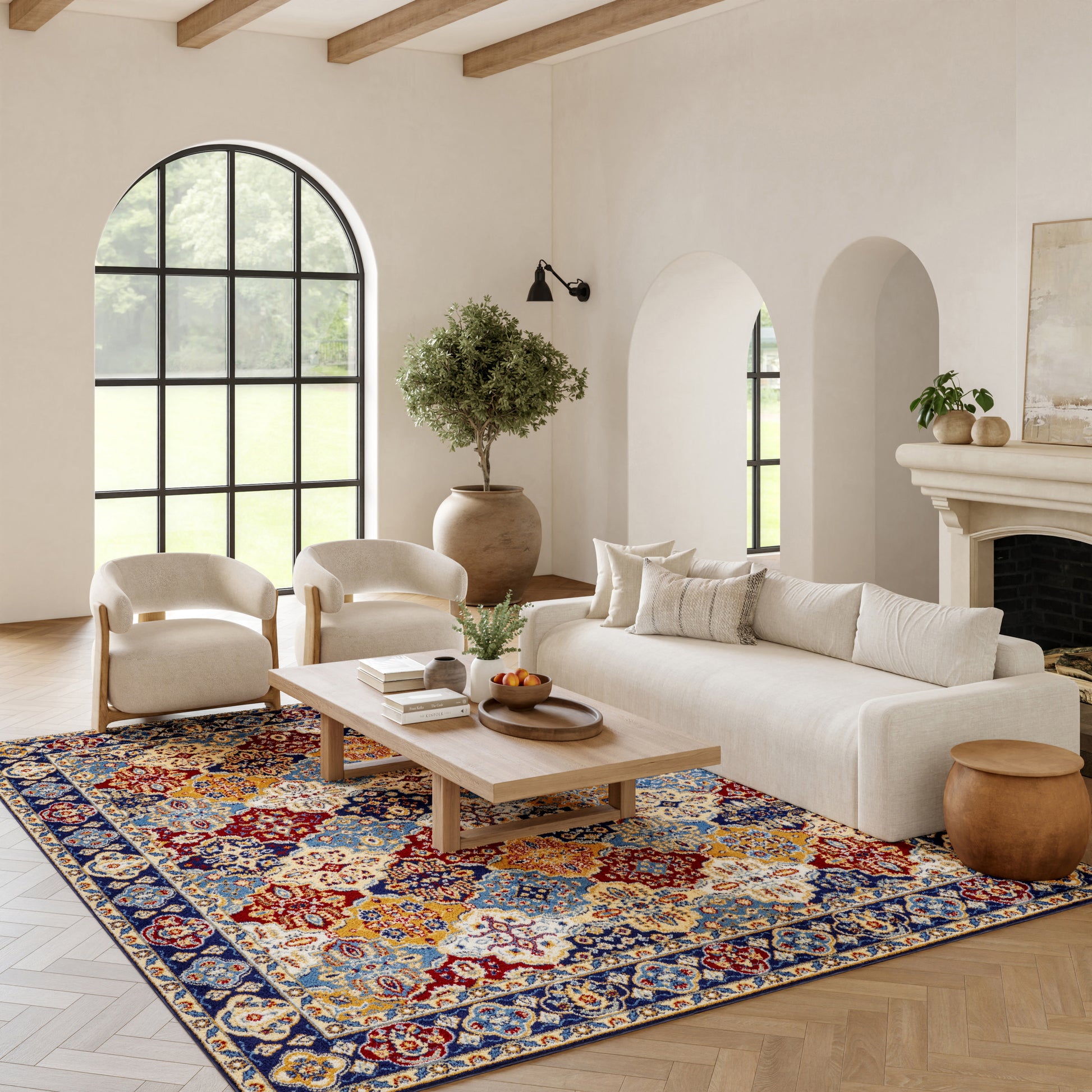 Neutral living room with arched window, beige sofa, two cream chairs, wooden coffee table, colorful rug, potted tree.