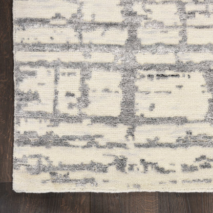 Cream & gray distressed abstract patterned rug with blocky shapes on hardwood floor.